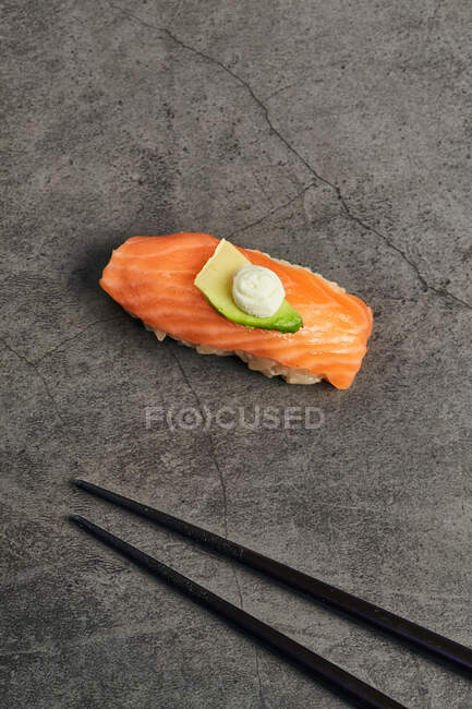 Alto ángulo de sushi nigiri sabroso con rebanada de salmón sobre arroz cubierto con rebanada delgada de aguacate y queso crema servido cerca de palillos - foto de stock