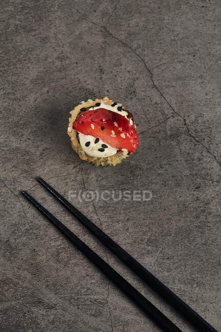 High angle of fried roll of Japanese sushi roll with sesame and strawberry slice near bamboo sticks — Stock Photo