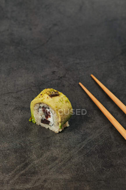 High angle of appetizing traditional Japanese sushi roll with rice avocado cream cheese placed with chopsticks — Stock Photo
