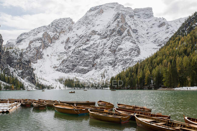 Paisaje de barcos de madera amarrados en un tranquilo lago ondulado rodeado de montañas nevadas y árboles de coníferas - foto de stock
