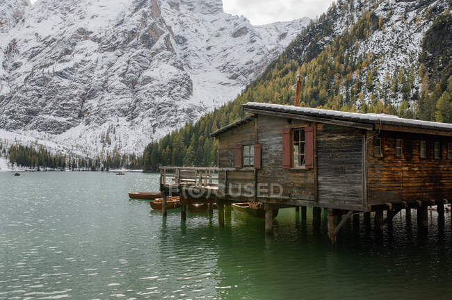 Cabaña de madera en un lago ondulado rodeado de bosques de coníferas y empinadas laderas de montaña en Italia - foto de stock