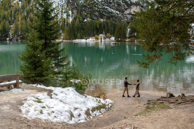 Vista lateral do casal em roupa exterior caminhando ao longo do lago Lago di Braies, no planalto da Itália — Fotografia de Stock