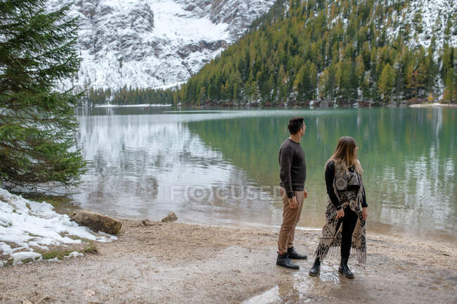 Vue latérale du couple en vêtements de dessus debout le long du lac Lago di Braies dans les hauts plateaux d'Italie — Photo de stock