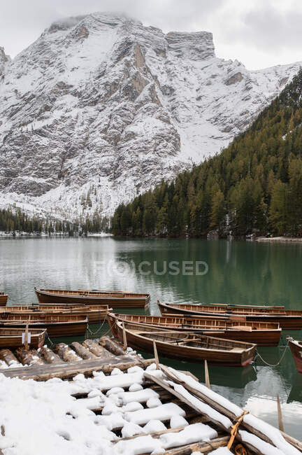 Декорації дерев'яних човнів, облаштованих на спокійному розпалі озера в оточенні засніжених гір і хвойних дерев — стокове фото
