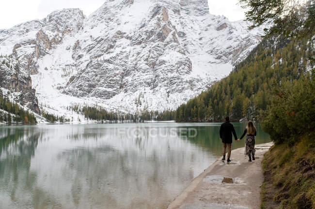 Retrovisore di coppia irriconoscibile in capispalla passeggiando lungo il lago di Braies nell'altopiano d'Italia — Foto stock