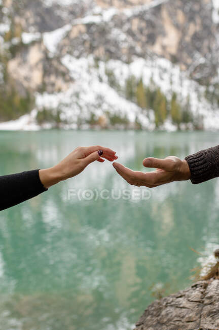 Crop anonymous traveler holding hand with girlfriend while supporting for climbing on rocky shore of Lago di Braies lake in Italy — Stock Photo