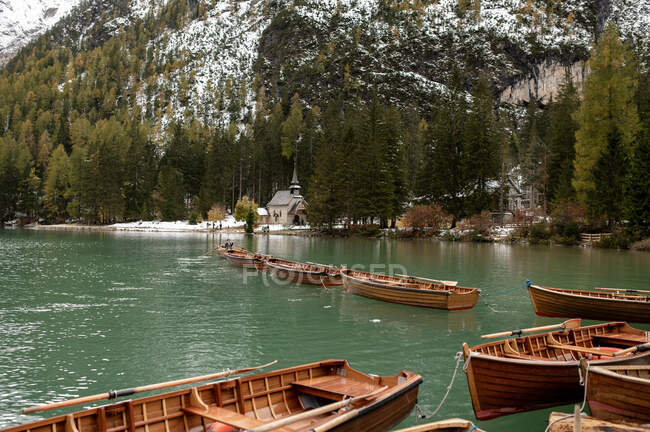 Scenery of wooden boats moored on calm rippling lake surrounded by snowy mountains and coniferous trees — Stock Photo