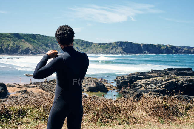 Vista posterior de un atleta masculino irreconocible admirando el mar ondeando en un día soleado sin nubes - foto de stock