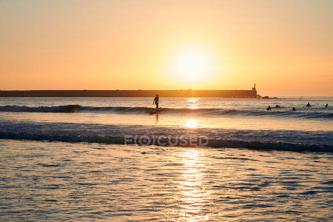 Silhouettes of people swimming and surfing in waves of sea under bright sun shining on sundown sky — Stock Photo