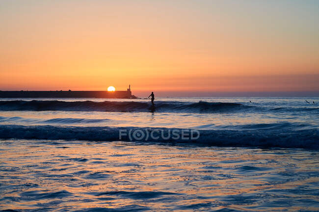 Silhouettes of people swimming and surfing in waves of sea under bright sun shining on sundown sky — Stock Photo