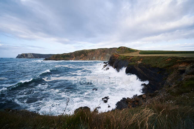 Paysage pittoresque de côtes escarpées rocheuses recouvertes d'herbe lavée par des vagues éclaboussantes — Photo de stock