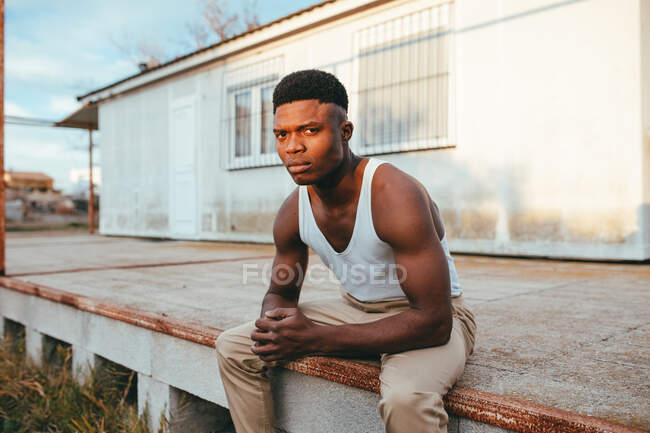 Young masculine African American male in undershirt with clasped hands looking at camera against house — Stock Photo