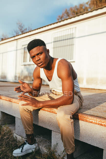 Молодой афроамериканец в майке с сжатыми руками смотрит в камеру напротив дома — стоковое фото
