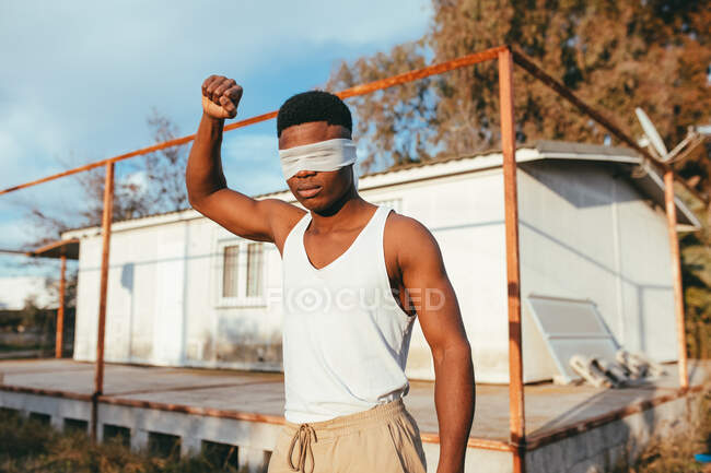 Анонимный мужчина-протестующий в майке и с завязанными глазами, стоящий с поднятой рукой в сельской местности — стоковое фото
