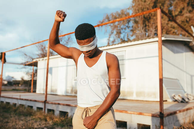 Manifestante masculino masculino anónimo en camiseta y venda en pie con el brazo levantado en el campo - foto de stock