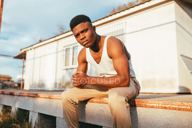 Giovane maschio afroamericano maschile in maglietta con le mani giunte guardando la fotocamera contro la casa — Foto stock