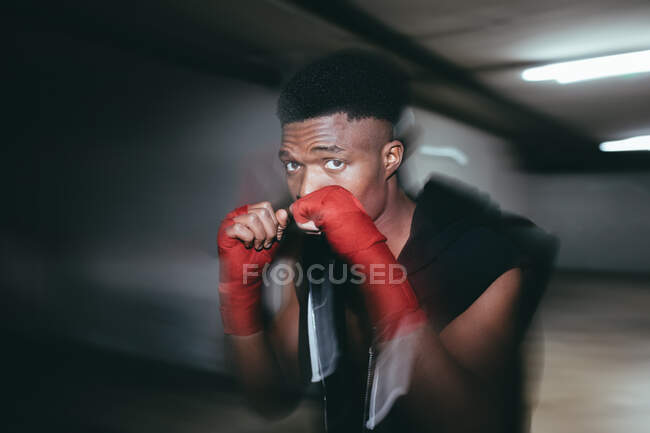 Junger starker afroamerikanischer Sportler in Boxhandschuhen beim Training und beim Blick in die Kamera im Gebäude — Stockfoto