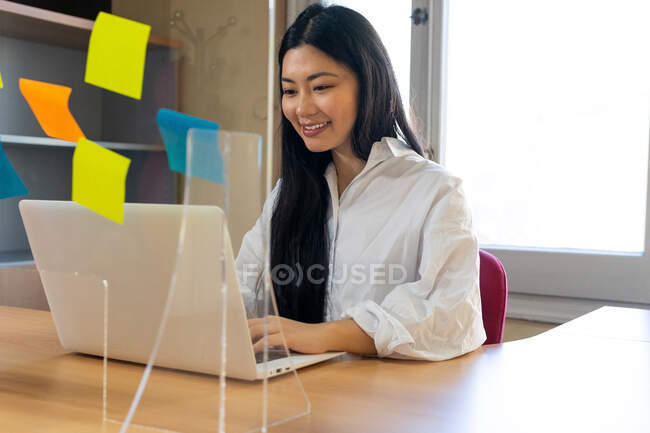 Feliz mujer étnica autónoma autónoma en gafas que trabajan en el ordenador portátil en casa - foto de stock