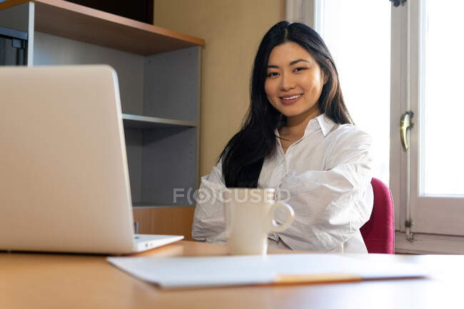 Mujer étnica emprendedora navegar netbook mientras se sienta con documento en papel - foto de stock