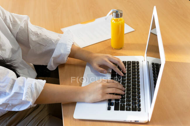 Culture femme entrepreneur navigation netbook tout en étant assis avec document papier et bouteille en verre respectueux de l'environnement de jus frais — Photo de stock