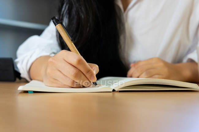Recadrer des informations d'écriture féminines anonymes dans un bloc-notes tout en étant assis à table et en travaillant à la maison — Photo de stock