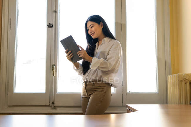 Jeune entrepreneur ethnique de contenu féminin en vêtements décontractés intelligents avec journal debout près du bureau le jour ensoleillé — Photo de stock