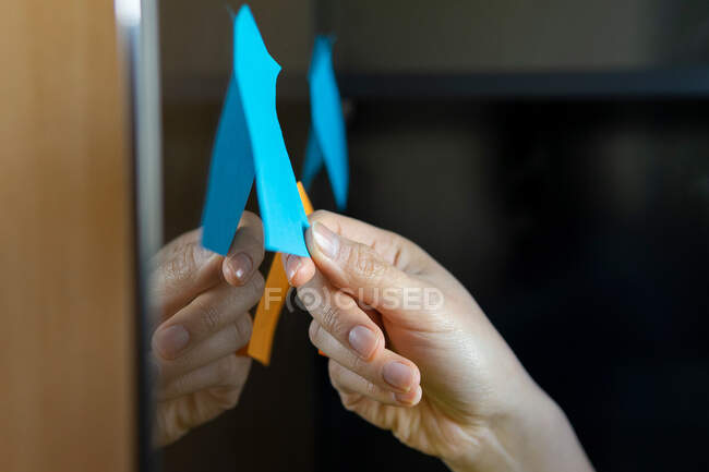 Crop executive anonimo prendere appunti su adesivi di carta brillante sulla parete di vetro in ufficio — Foto stock