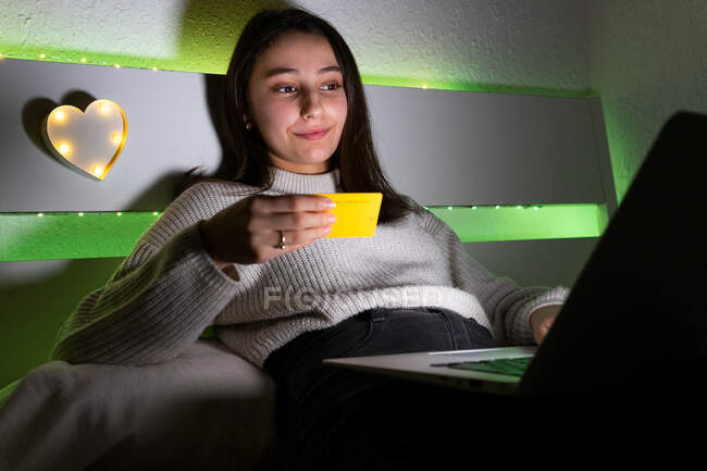 Side view teen in sweater typing credit card data on keyboard of netbook while shopping online — Stock Photo