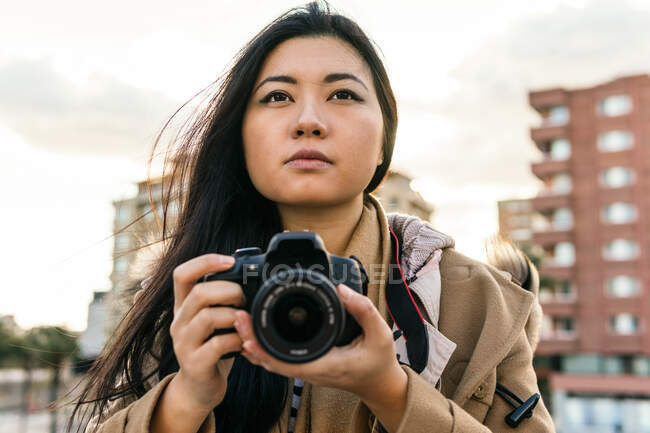 Етнічний азіатський фотограф знімає фотографію на професійній фотокамері на вулиці міста — стокове фото