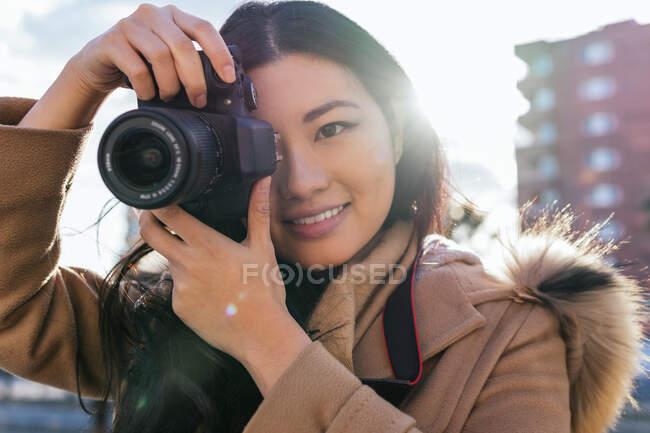 Étnico joven feliz asiático mujer fotógrafo disparo foto en profesional cámara de fotos en la calle de la ciudad - foto de stock