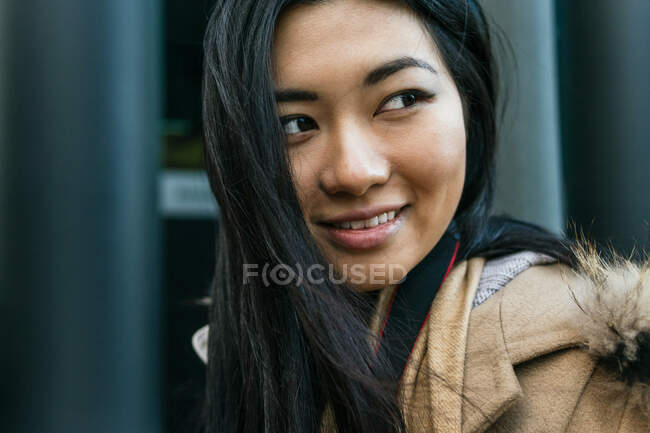 Mulher étnica positiva em outerwear quente em pé na rua olhando para longe — Fotografia de Stock