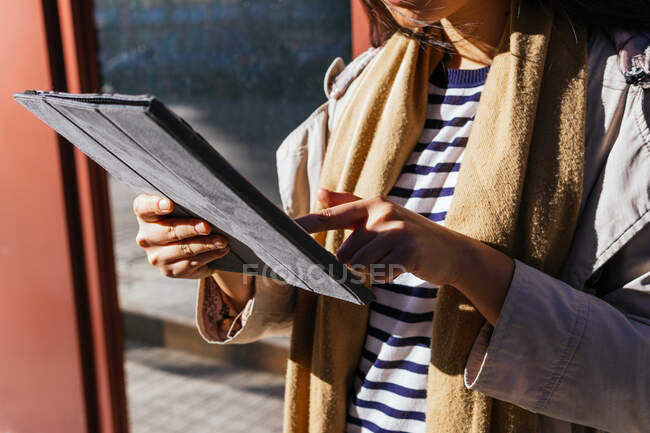 Cropped unrecognizable female standing against reflecting mirrored wall and browsing gadget on sidewalk in sunny day — Stock Photo