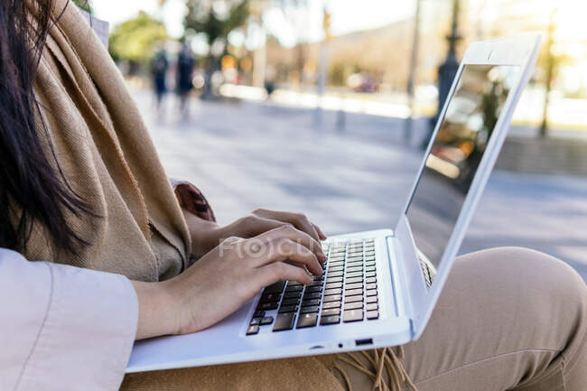 Recortado irreconocible mujer usando ropa interior caliente netbook de navegación mientras trabajaba remotamente sentado en un banco en la calle - foto de stock