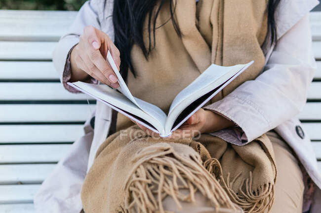 Обрезанная неузнаваемая женская книга для чтения, сидящая на скамейке — стоковое фото