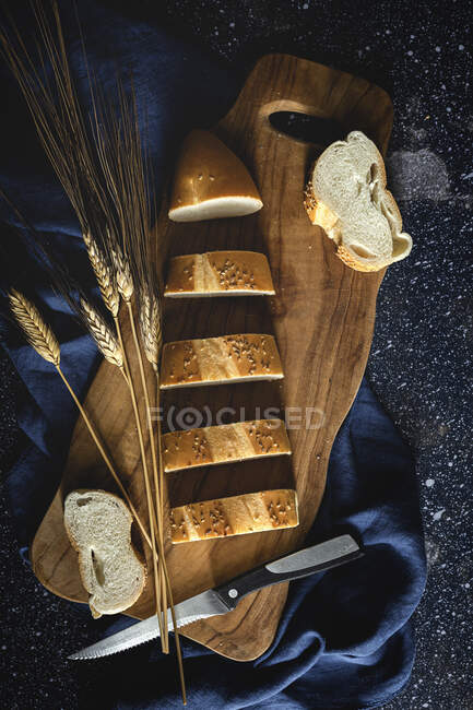 Top view of pieces of white bread near knife and wheat spikes on wooden board — Stock Photo