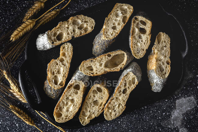 From above of appetizing crusty bread near wheat spikes and dark fabric on table — Stock Photo