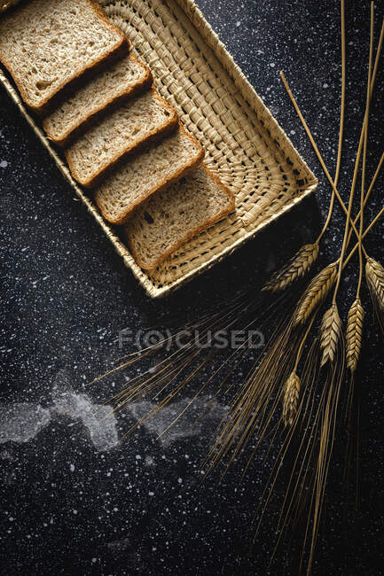 Vista dall'alto del pane di segale fresco fatto in casa vicino a coltello in cesto di vimini e spuntoni di grano sul tavolo — Foto stock