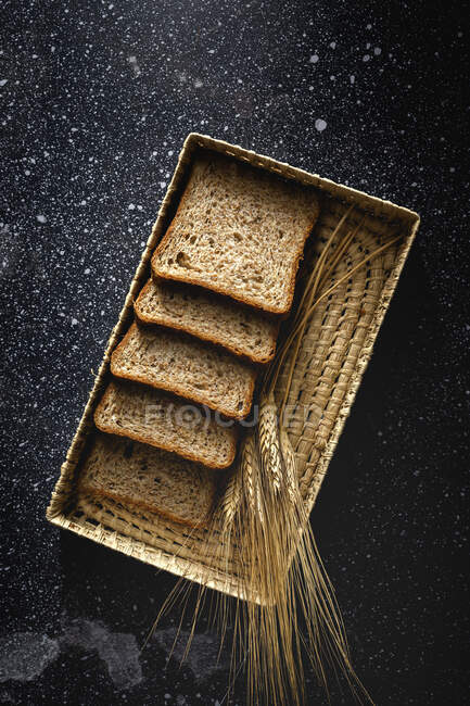 Top view of fresh homemade rye bread near knife in wicker basket and wheat spikes on table — Stock Photo