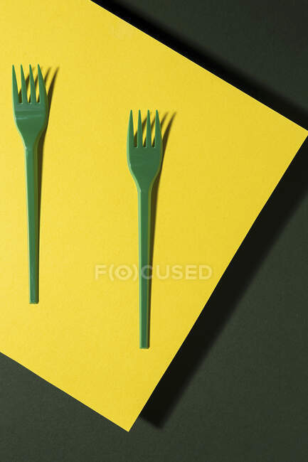 Vista aérea de tenedor ecológico verde brillante cerca de la hoja de cartón amarillo sobre fondo verde - foto de stock