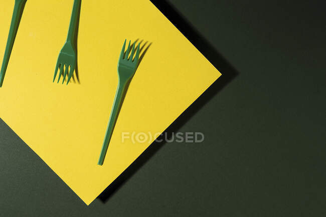 Overhead view of bright green eco friendly fork near yellow carton sheet on green background — Stock Photo