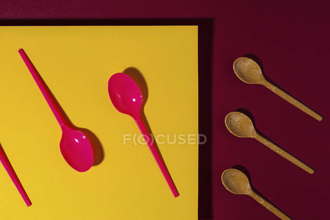 Overhead view of bright red and brown eco friendly spoons near yellow carton sheet — Stock Photo
