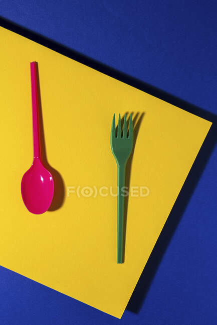 Overhead view of bright colorful eco friendly cutlery near yellow carton sheet — Stock Photo