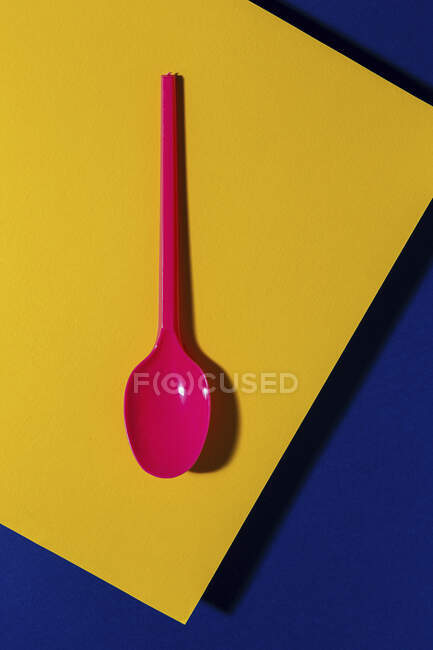 Vista aerea di rosa ecologico cucchiaio vicino giallo e blu foglio di cartone sfondo — Foto stock