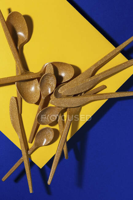 Overhead view of brown eco friendly cutlery near yellow and blue carton sheet background — Stock Photo