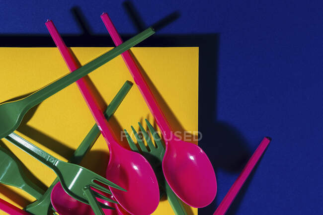 Вид зверху яскравих барвистих екологічно чистих столових приборів біля жовтого картонного листа — стокове фото