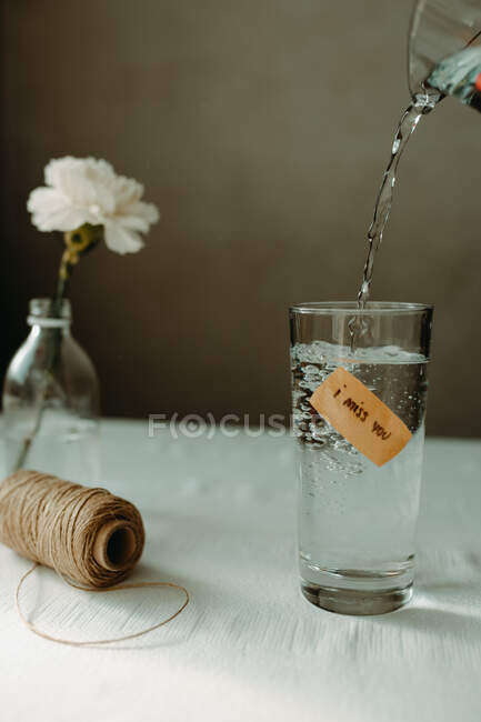 Вода, що вливається в скляний посуд з написом, я сумую за тим, що ви помістили біля шпагату нитки і квітучої гвоздики — стокове фото