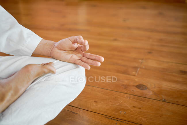 Crop anonymous male in white clothes doing mudra gesture with hands while practicing yoga in house — Stock Photo