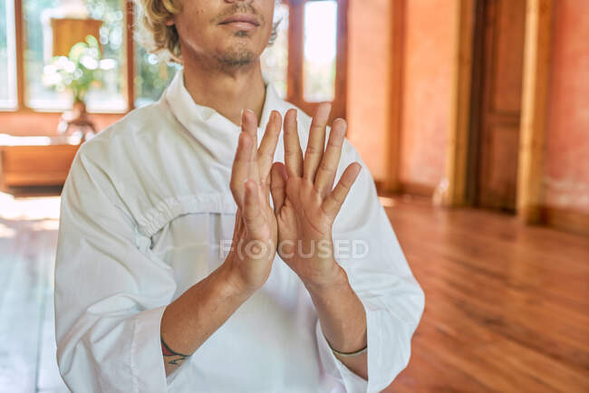 Crop anonymous unshaven male in white clothes touching thumbs while practicing yoga in house — Stock Photo