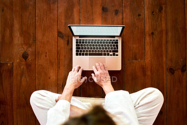 D'en haut recadré mâle concentré méconnaissable assis avec les jambes croisées navigation sur netbook dans la salle de méditation tout en pratiquant le yoga — Photo de stock