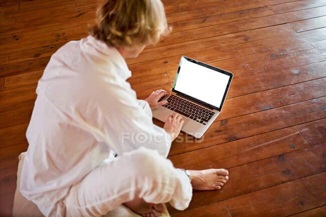Joven macho concentrado sentado con las piernas cruzadas navegando en netbook en la sala de meditación mientras practica yoga - foto de stock